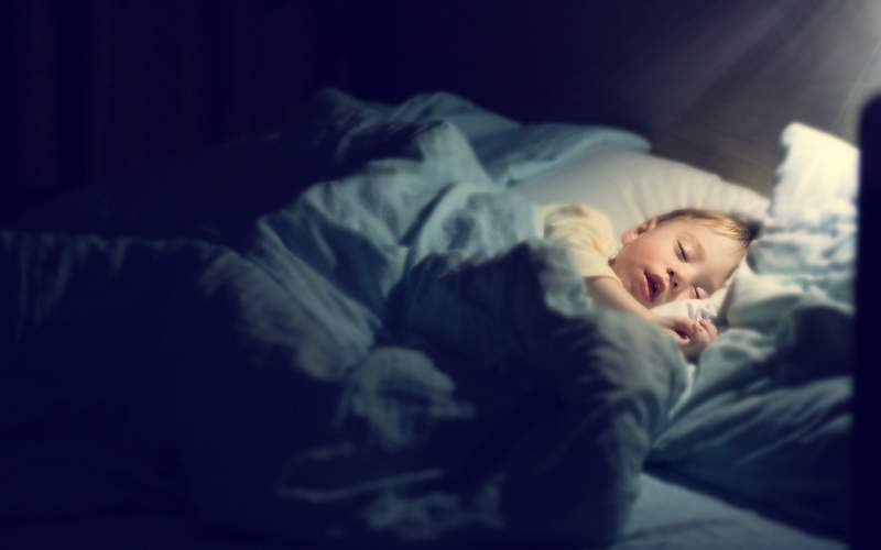 Boy asleep in his bed with a small lamp on