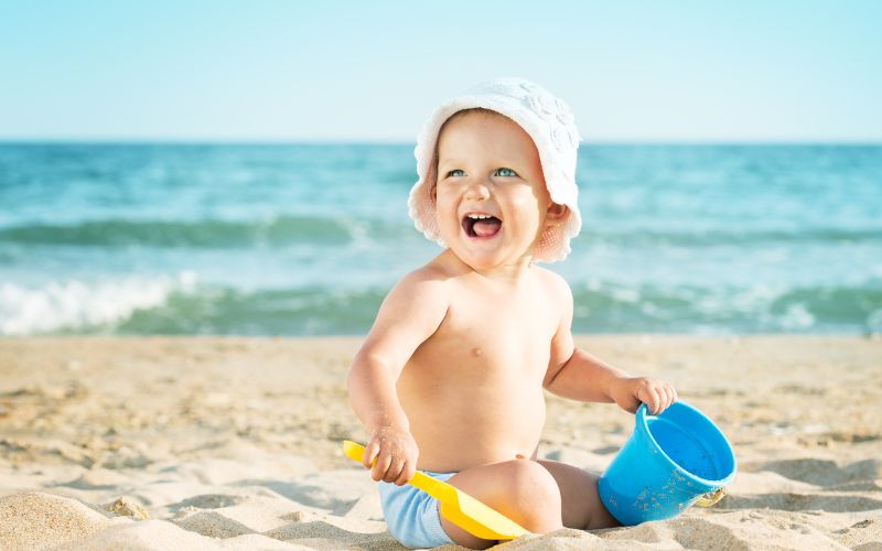 Baby sleep on holiday 1 Toddler sitting on the beach in a sunhat